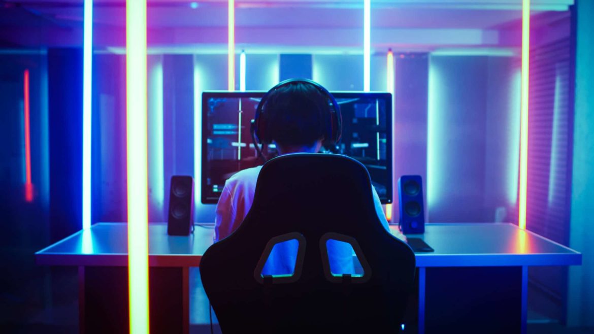 Back View Shot of the Beautiful Professional Gamer Girl Putting on Headset and Starts Playing Online Video Game on Her Personal Computer Cute Casual Geek Girl Lit by Neon Lamps in Retro Arcade Style
