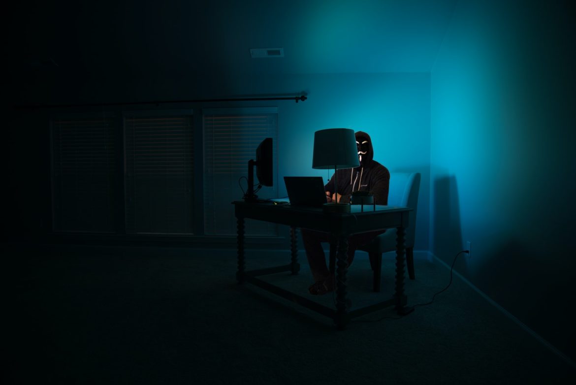 a man at a computer disguised as an anonymous hacker