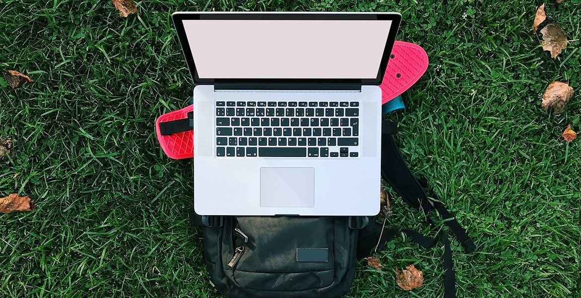 Laptop with blank white screen on top of skateboard and backpack on bright grass background at the park. Mobile office set up at Budapest park.