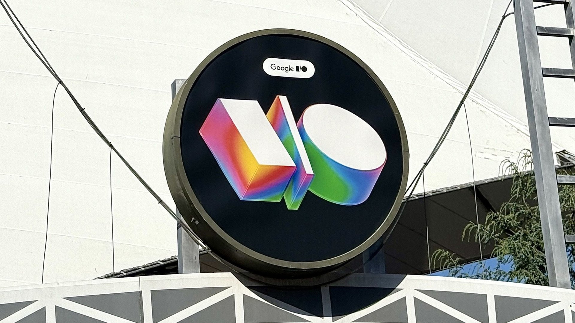 Circular black sign with colorful 3D letters MO on the front and a small Google label above