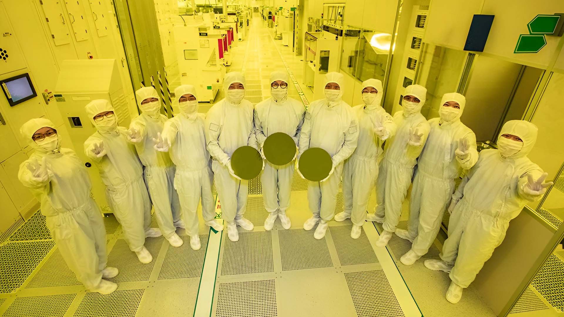 Group of scientists in white cleanroom suits posing in a high tech laboratory holding round wafer disks