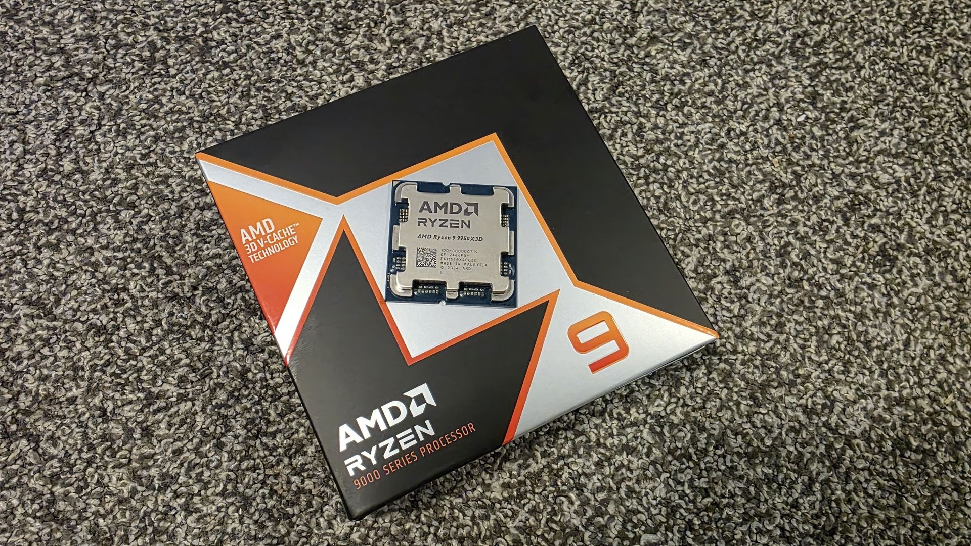 AMD Ryzen processor box on a textured gray carpet with the CPU resting on top of the packaging