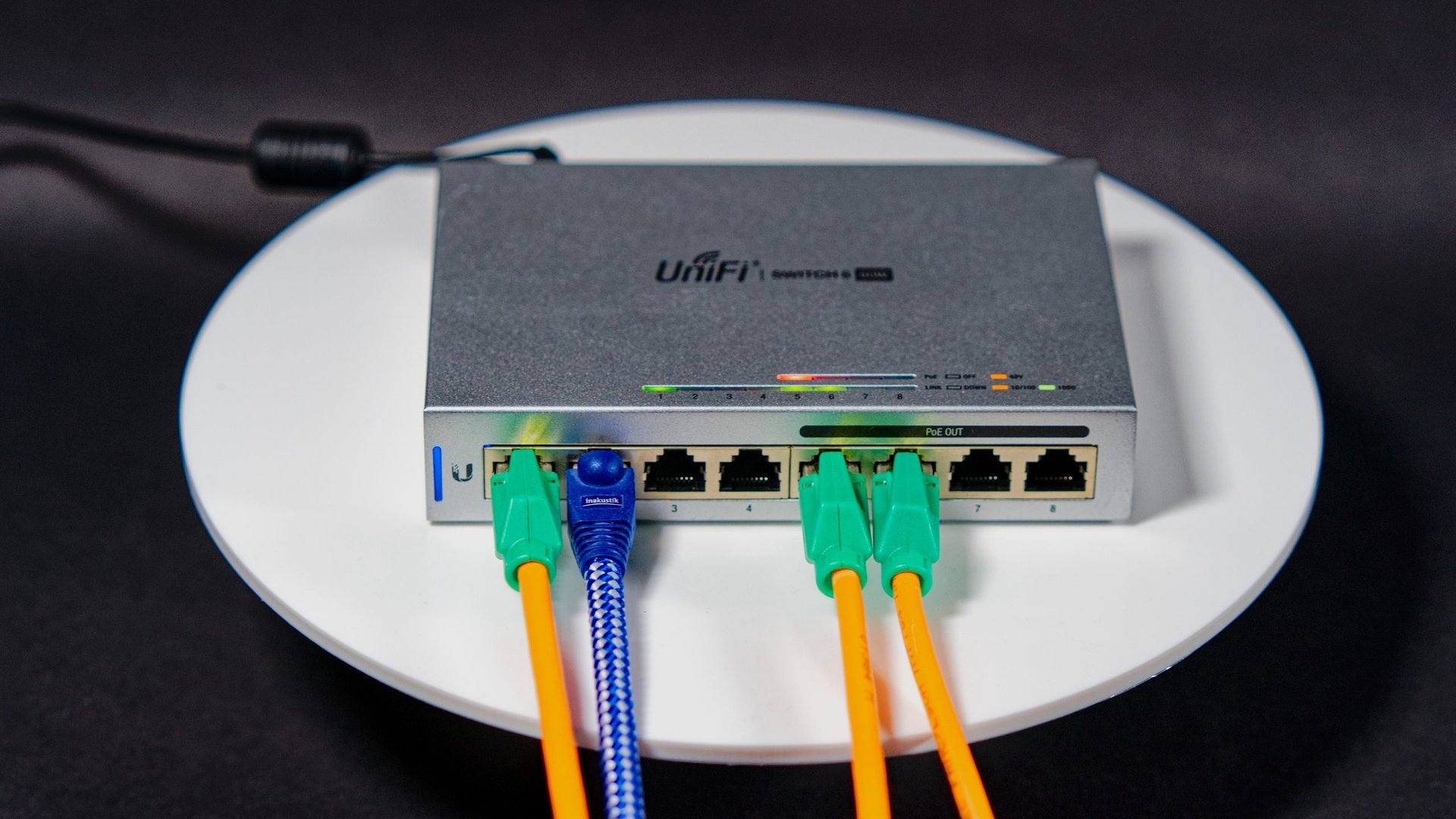 Unifi eight port network switch on a white circular table with multiple colored Ethernet cables plugged in