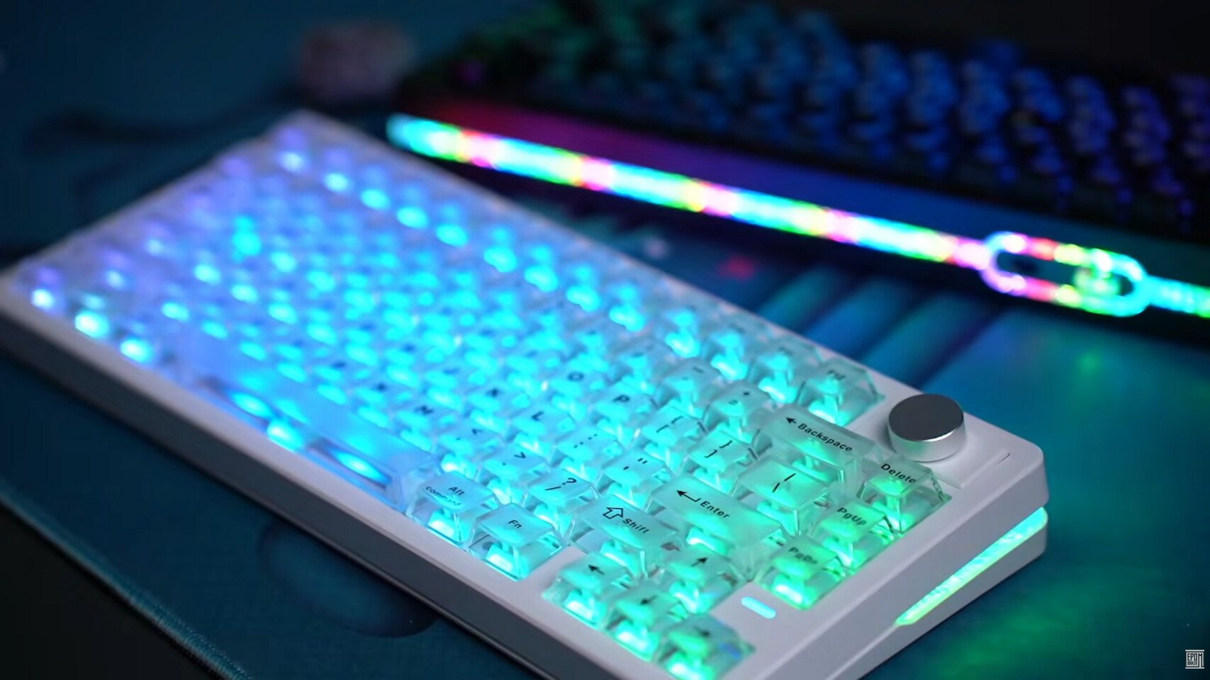 White mechanical keyboard with cyanblue backlighting and a silver trackball on the right RGB strip glowing in the background on a desk