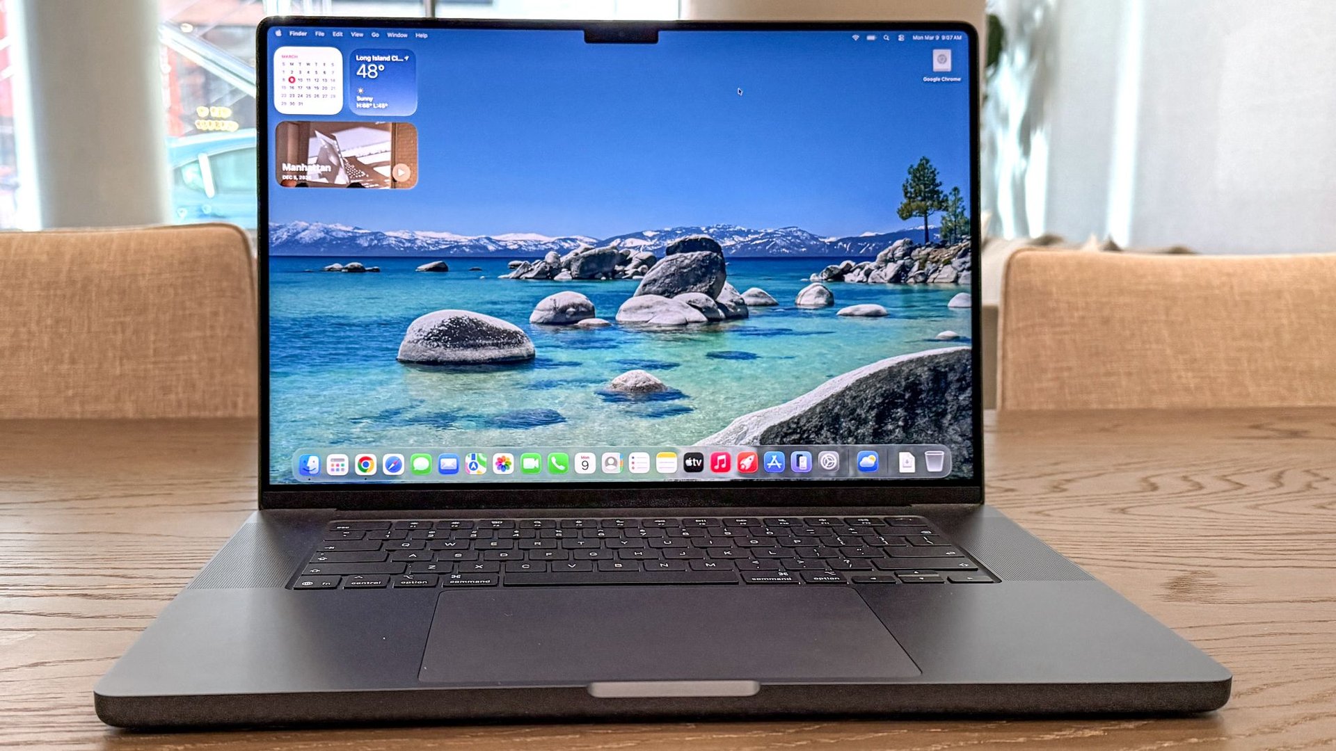 Open laptop on a wooden table displaying a beach wallpaper with turquoise water and rocks app dock visible at bottom