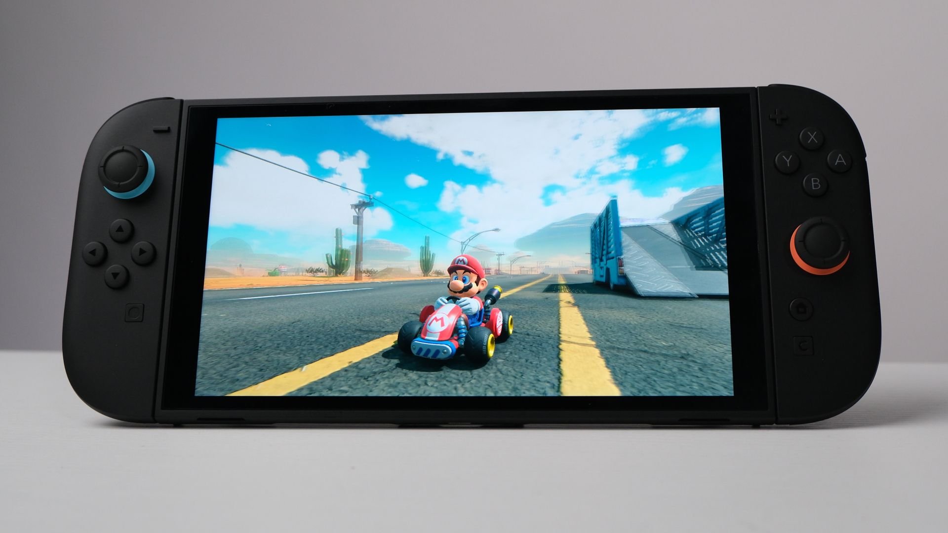 Handheld gaming console on a table displaying Mario Kart with Mario driving a red kart on a desert highway