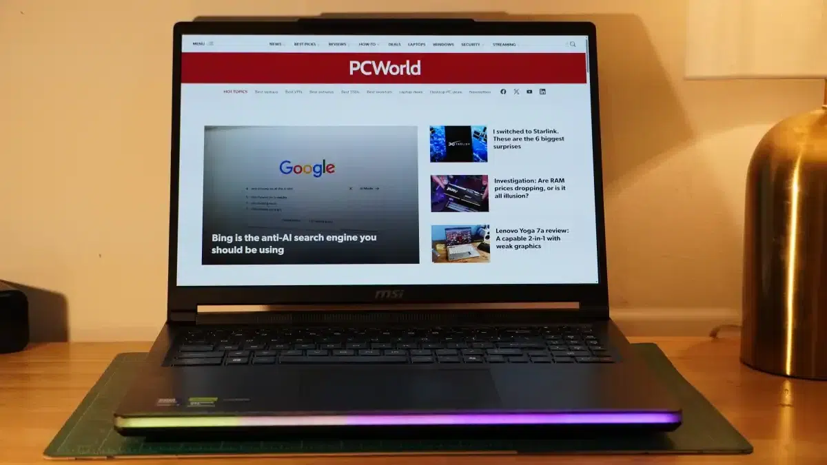 Laptop on a wooden desk displaying the PCWorld homepage with an article about Bing RGB light bar on the front edge of the laptop