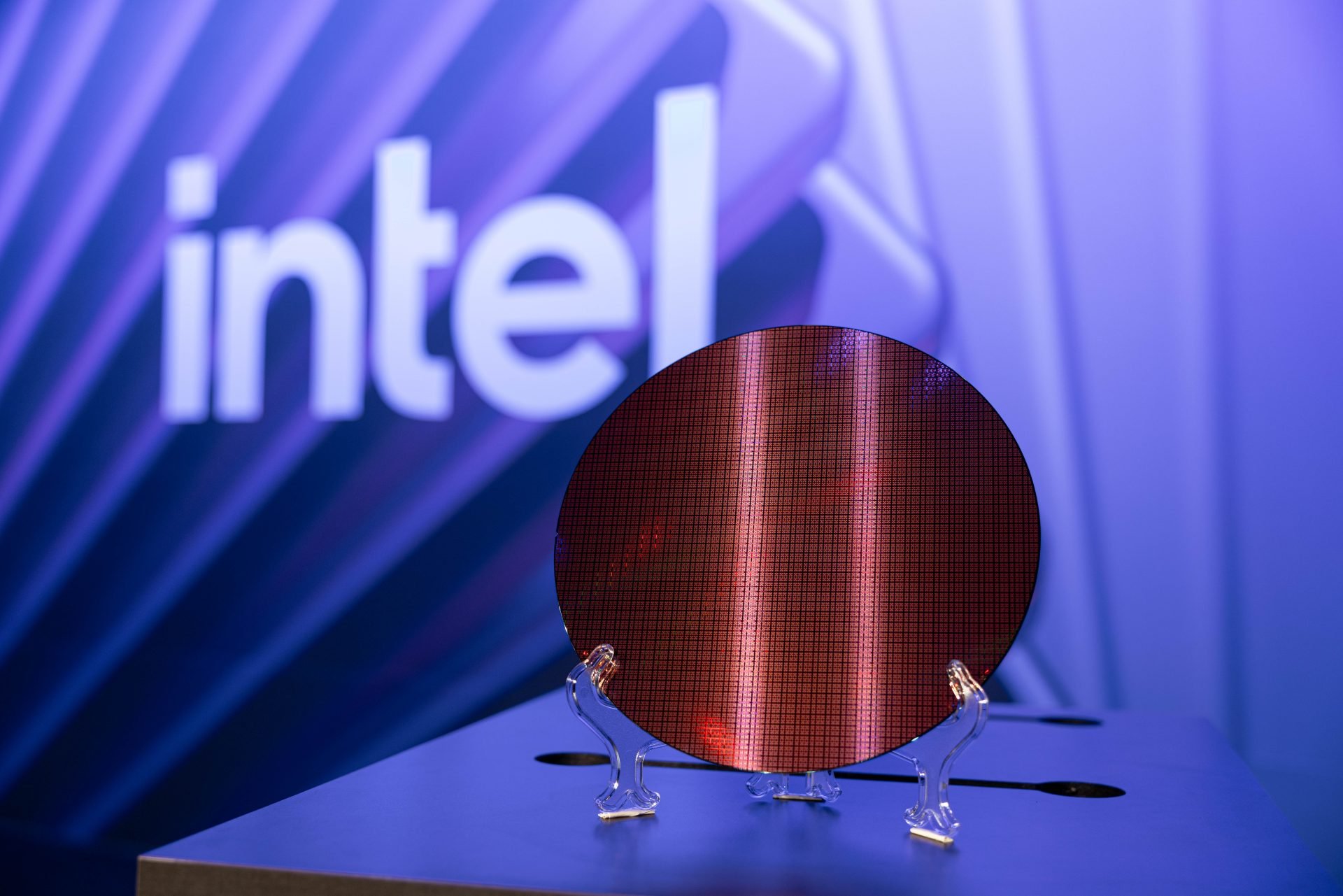 Red circular semiconductor wafer with grid pattern on a clear display stand against a blue background