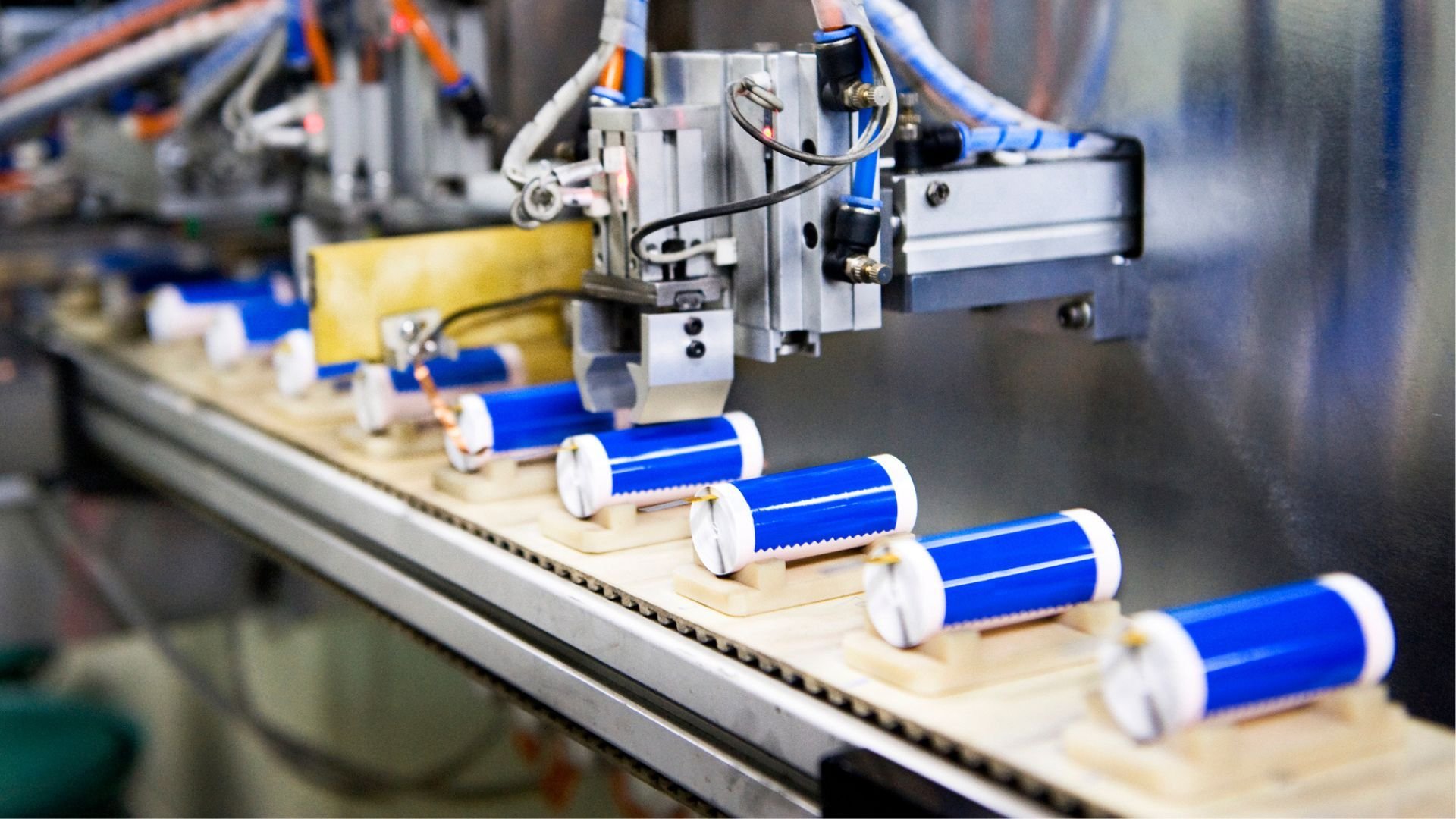 Automated production line with blue cylindrical rollers moving along a conveyor under a robotic head
