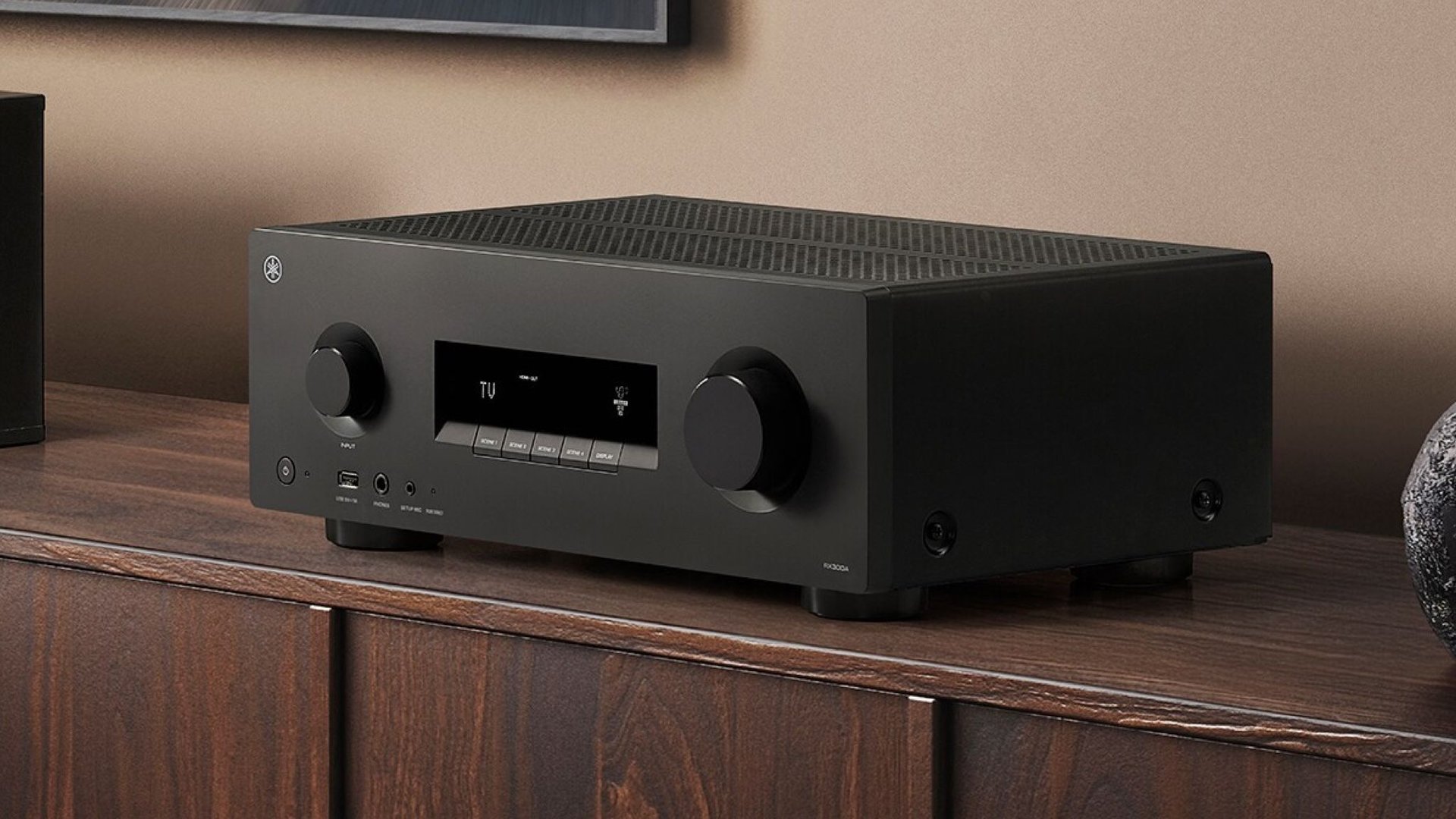 Black stereo amplifier on a wooden cabinet with a central digital display and two large front knobs