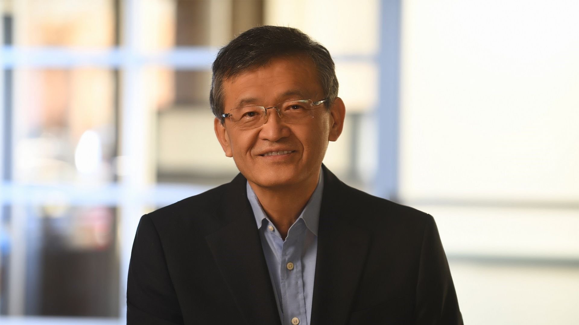 Portrait of a smiling Asian man in a dark blazer and light blue shirt indoor office background out of focus