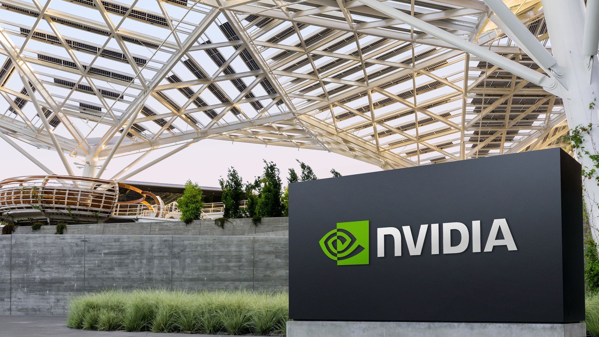 NVIDIA logo on a dark sign next to a white crisscross metal canopy and greenery in an outdoor area
