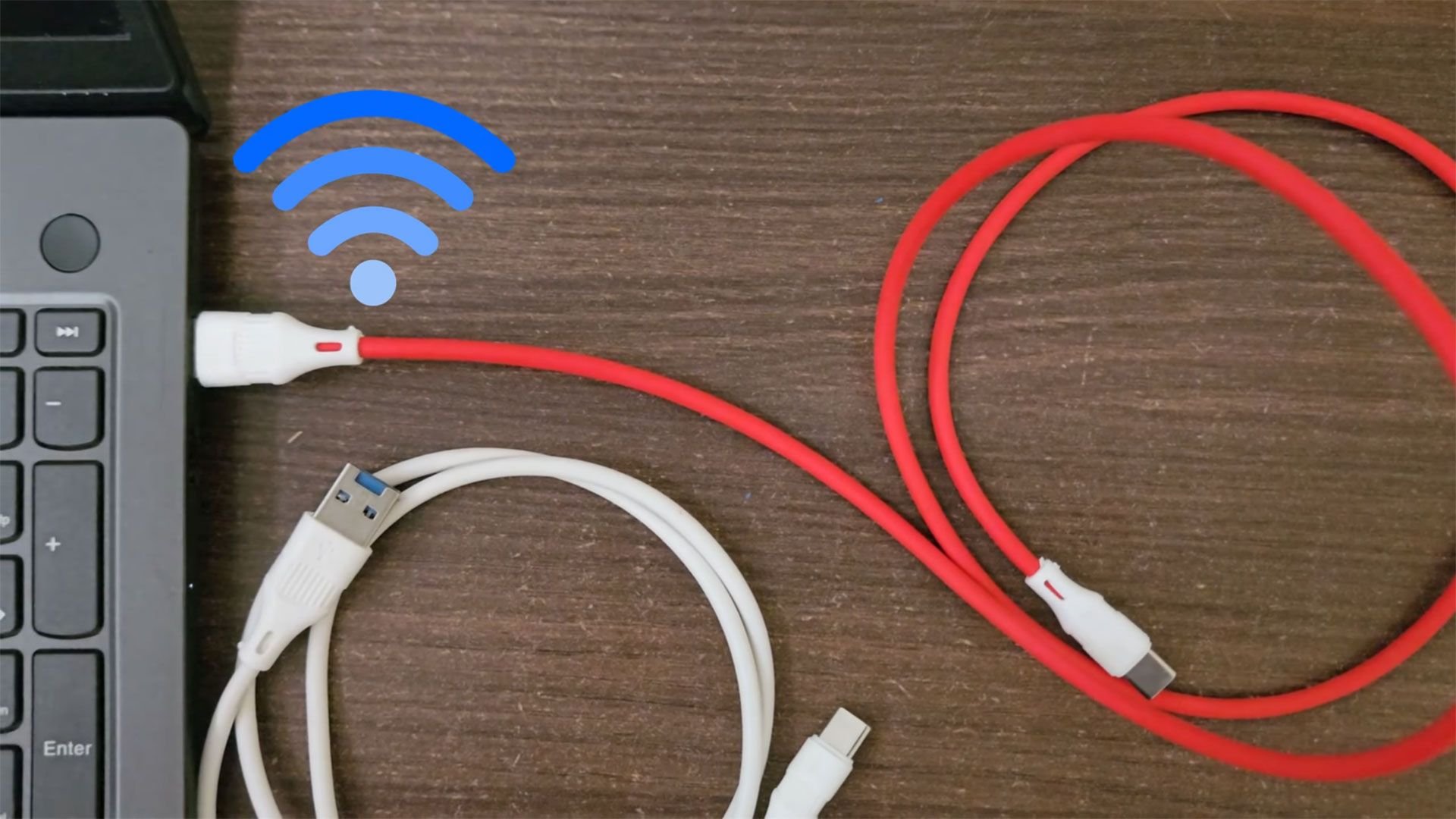 Close up of a laptop on a wooden desk with red USB C cables connected to its side and a white USB cable nearby