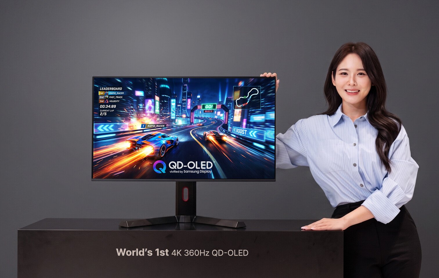 Woman presenting a Samsung QD OLED monitor showing a neon racing game on a desk