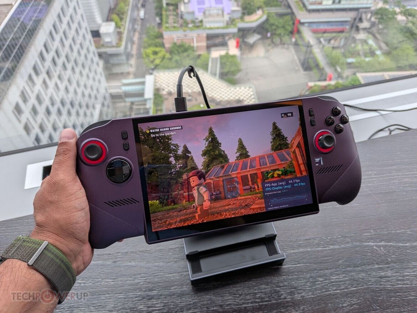 Person holds a purple handheld gaming console with side controllers playing a colorful outdoor game on a rooftop