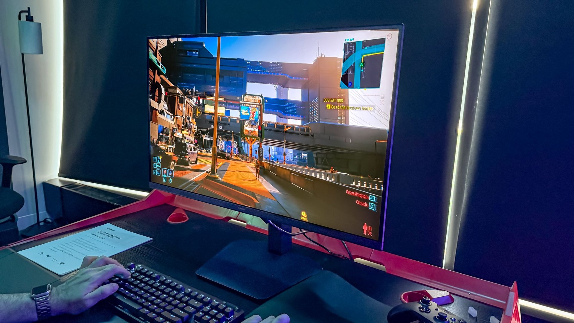 Gamers hands on keyboard and mouse in front of a large curved monitor displaying an urban shooter game