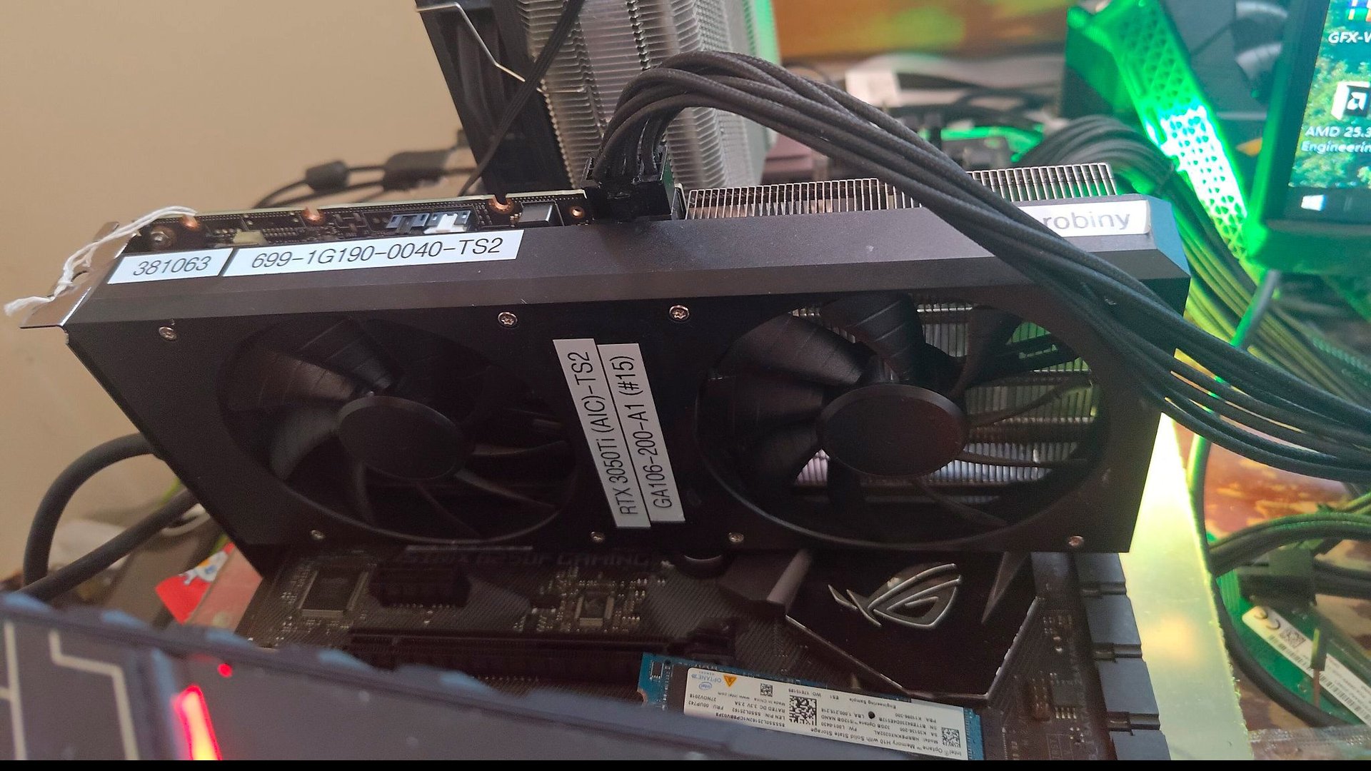 Graphics card with twin cooling fans inside a PC case labeled stickers and multiple power cables nearby
