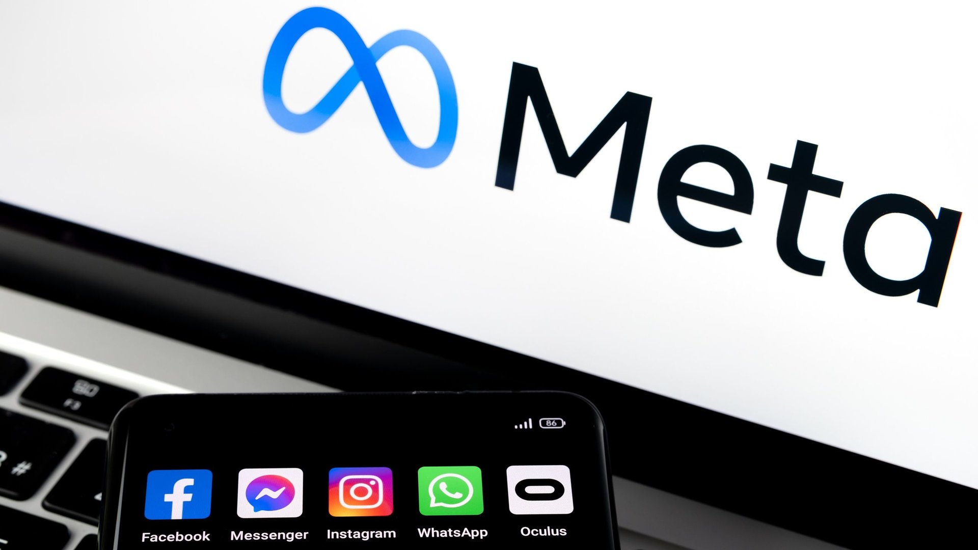 Close up of a laptop screen displaying the Meta logo with a smartphone showing social app icons Facebook Messenger Instagram WhatsApp Oculus