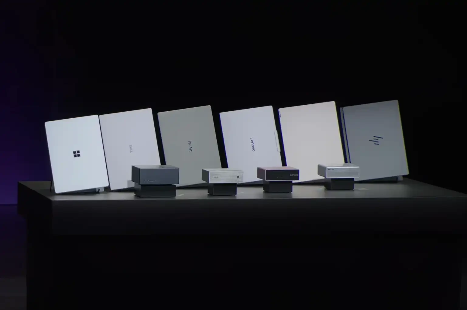 Row of laptops on a dark display table angled backs facing the viewer brands like Microsoft Dell Lenovo and HP are visible on the devices