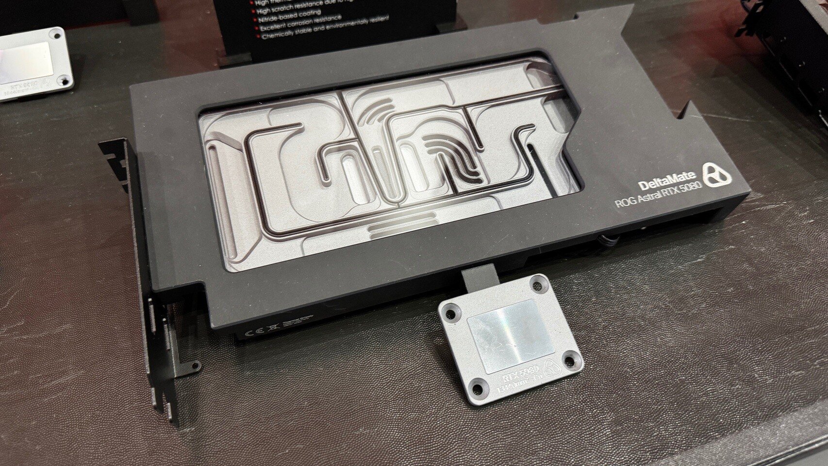 DeltaMate GPU water block with a separate mounting plate on a dark work surface branding visible on the block edge ROGRTX label