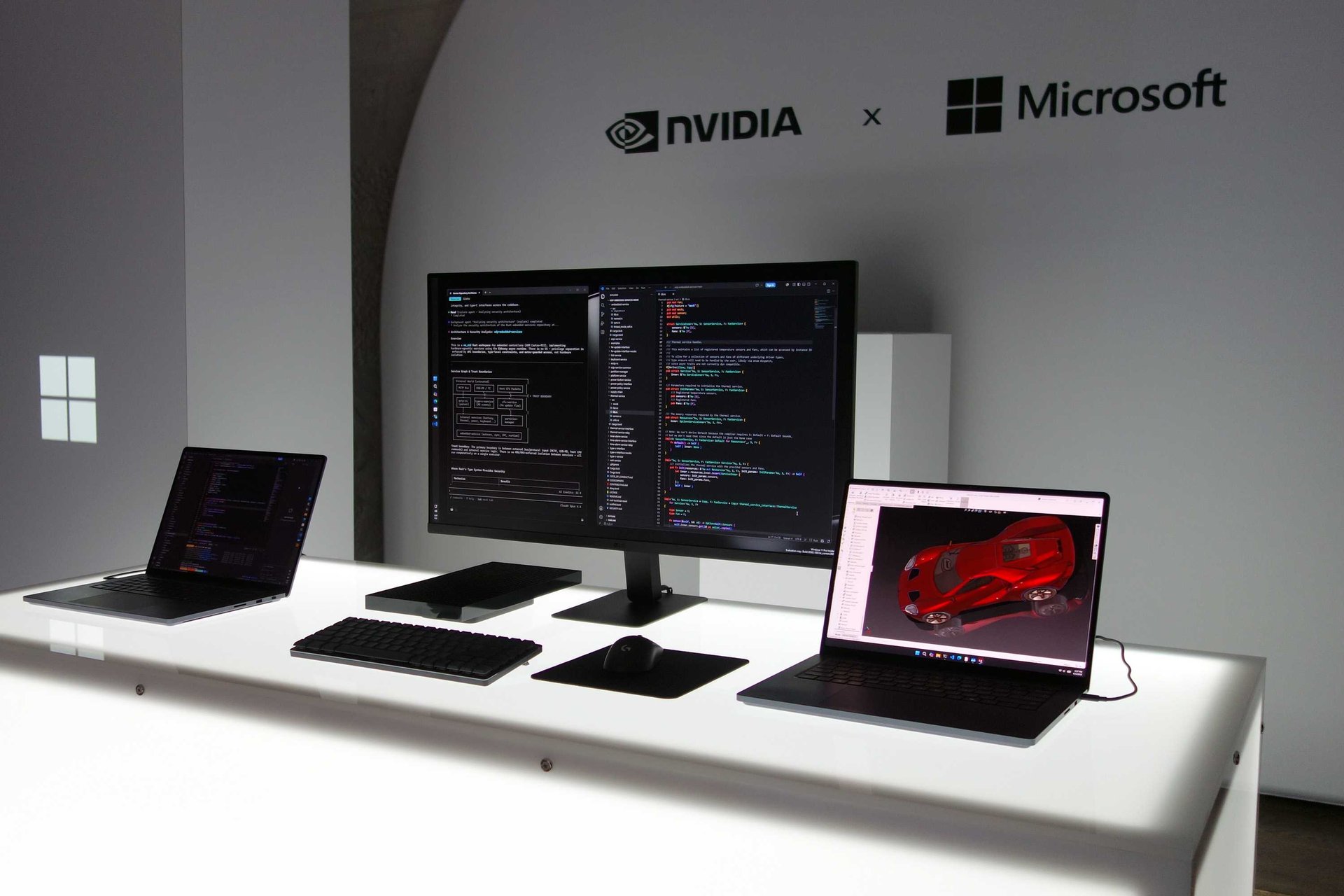 Workstation with three screens showing code and a red car image on the right laptop placed on a white desk under a wall featuring NVIDIA × Microsoft logos