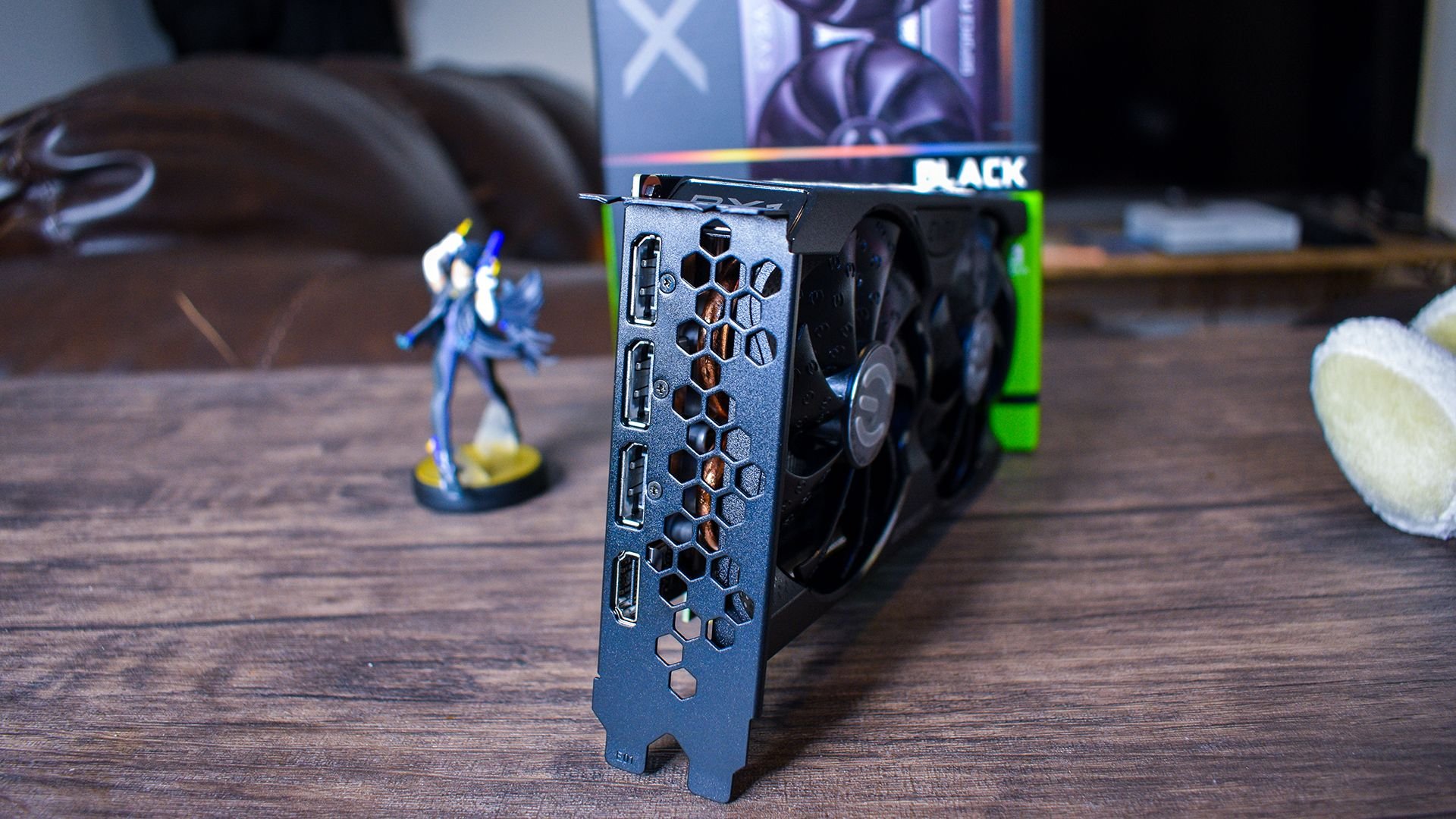 Close up of a graphics card with a honeycomb vent pattern standing on a wooden table with a blurred game box and toys in the background