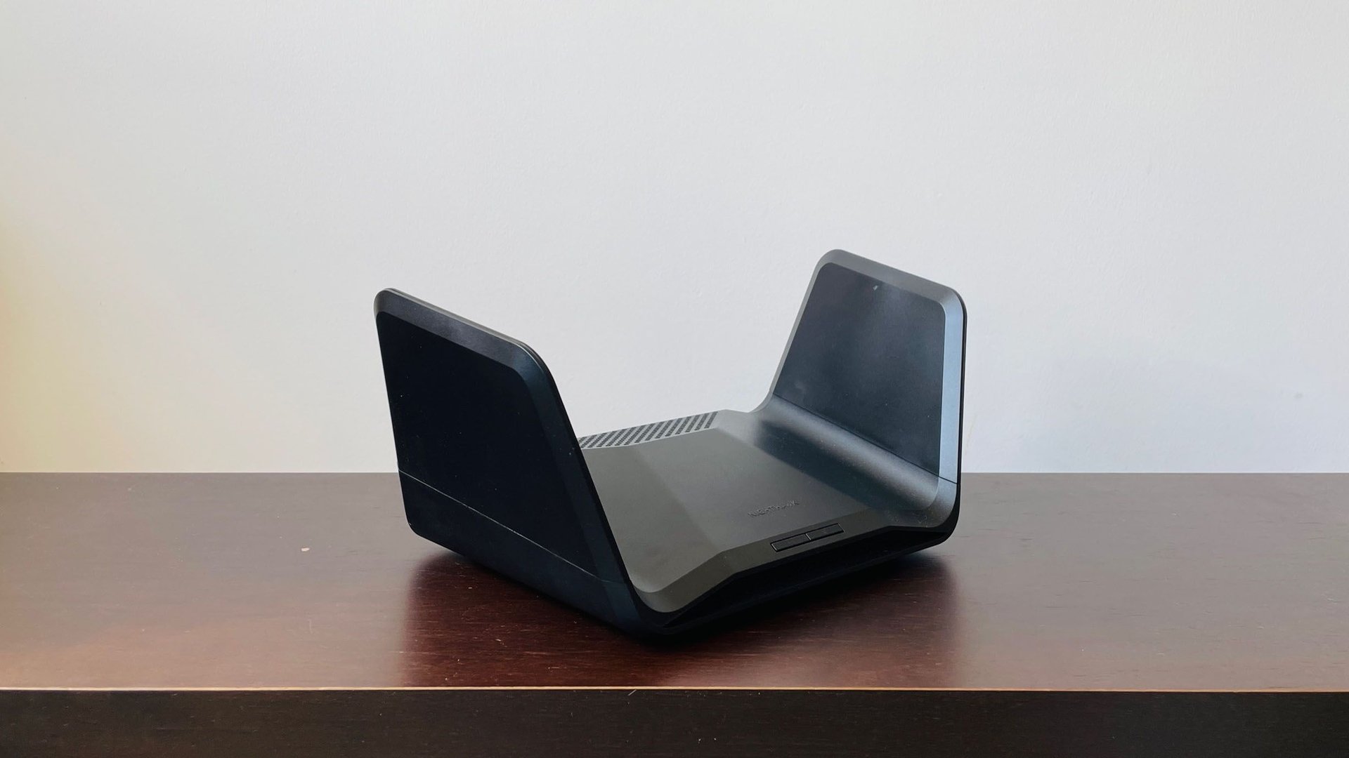 Black dualantenna WiFi router on a wooden table facing left with a vent on top and rounded edges