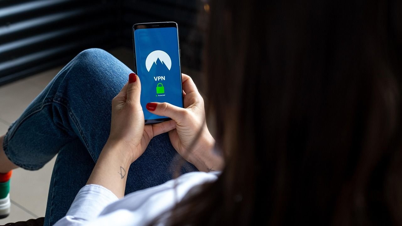 Person seated with legs crossed holding a phone displaying a VPN app screen with a mountain logo and green lock