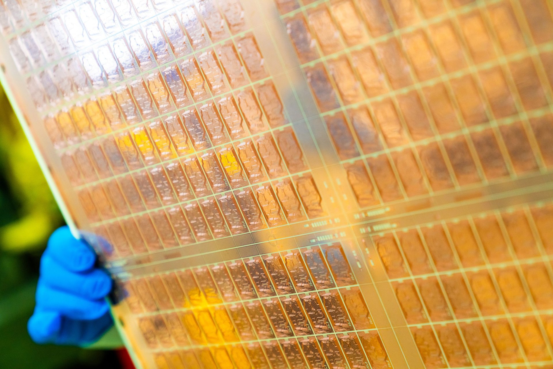 Close up of a silicon wafer with a grid of microchip patterns being held by a gloved hand
