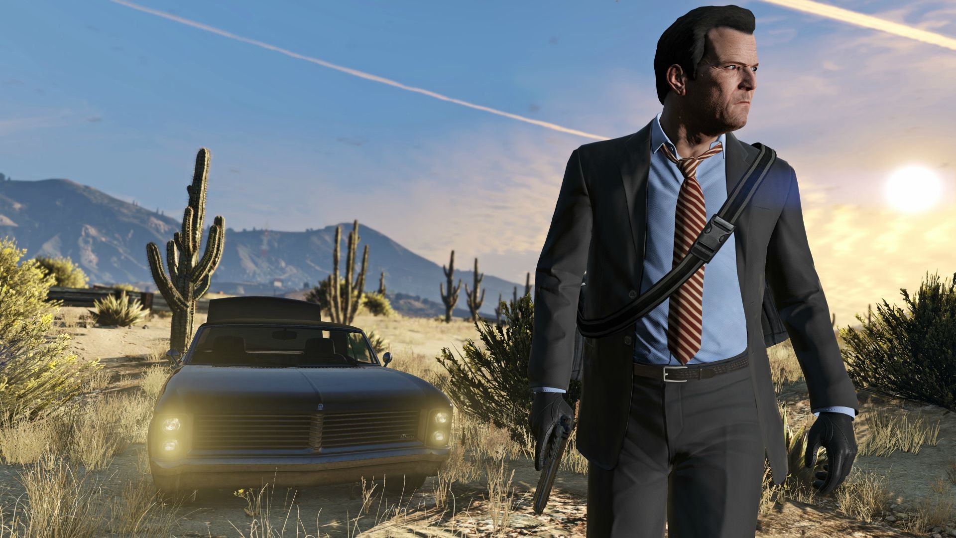 Man in a dark business suit with a red striped tie and a shoulder strap walks through a desert at sunset holding a pistol beside a vintage convertible car