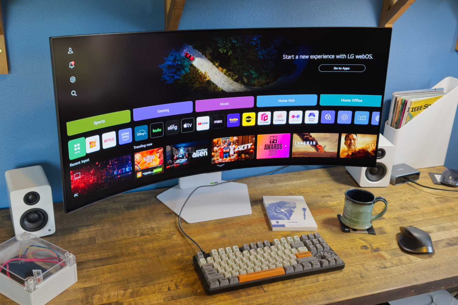 Curved widescreen monitor on a wooden desk showing a colorful app grid with icons keyboard and mouse nearby