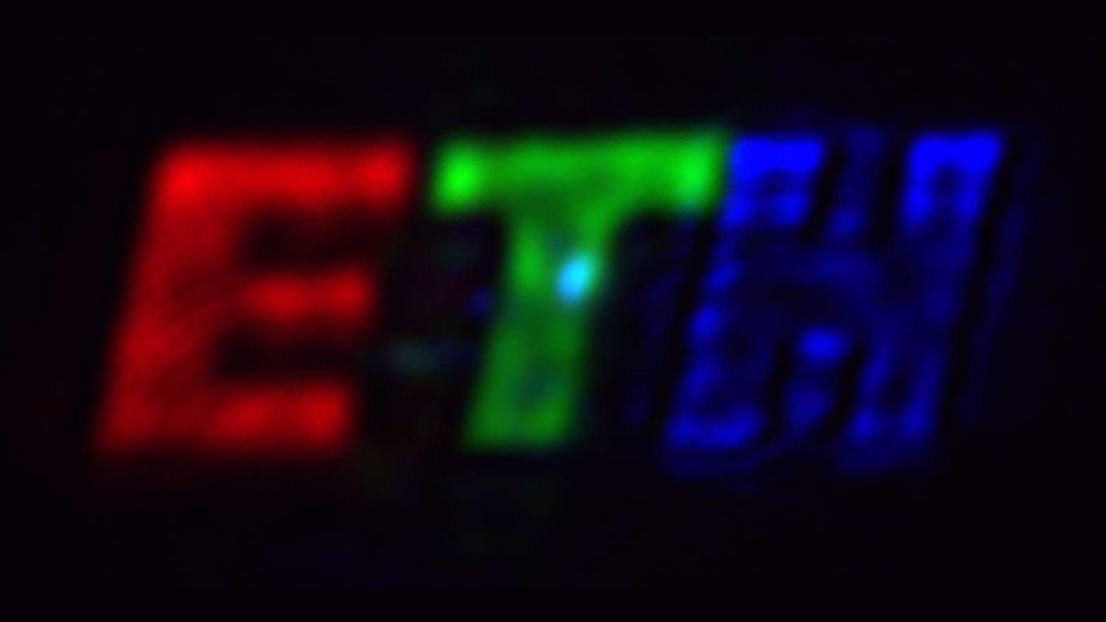Blurry neon sign showing red E green T and blue N on a dark background