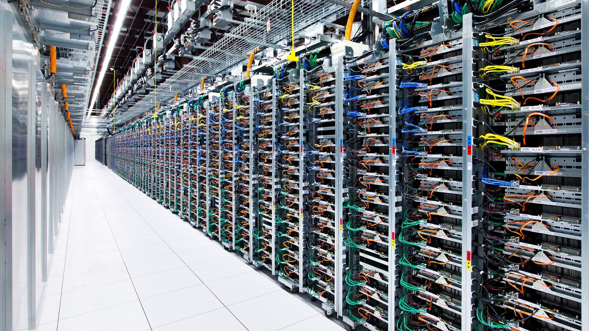 Rows of server racks in a data center with colorful network cables and overhead cabling