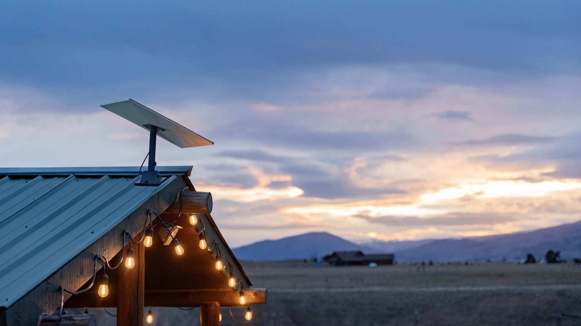 Rooftop pergola with hanging string lights at dusk solar panel on the roof wide open countryside and mountains in the background