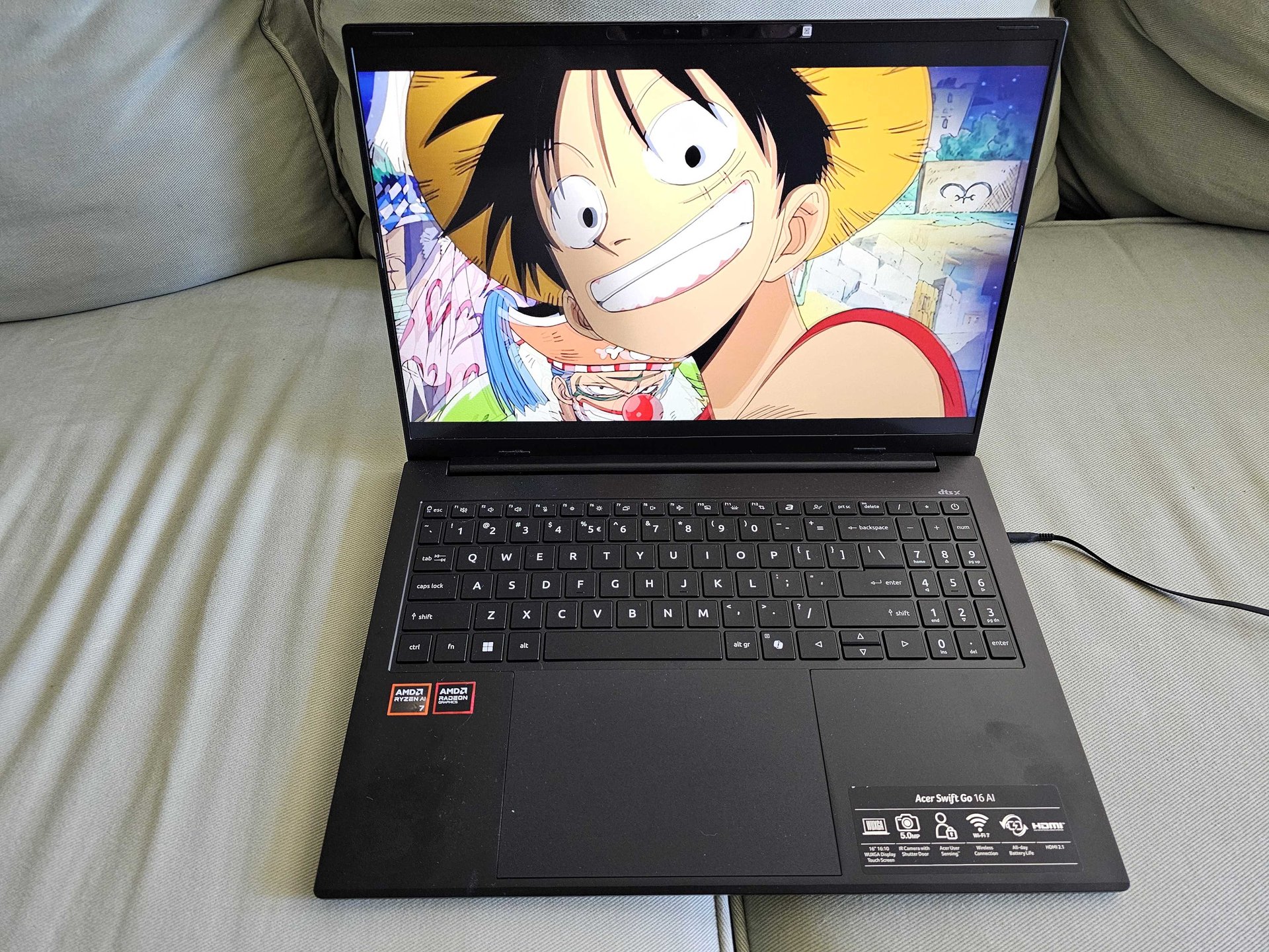 Laptop on a couch displaying a colorful One Piece wallpaper featuring Monkey D Luffy on the screen