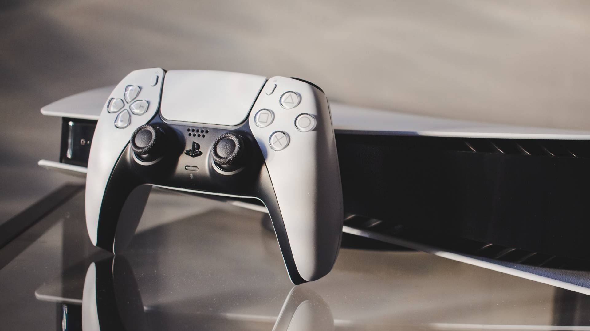 White PlayStation 5 DualSense controller resting on a glass surface with a blurred console in the background