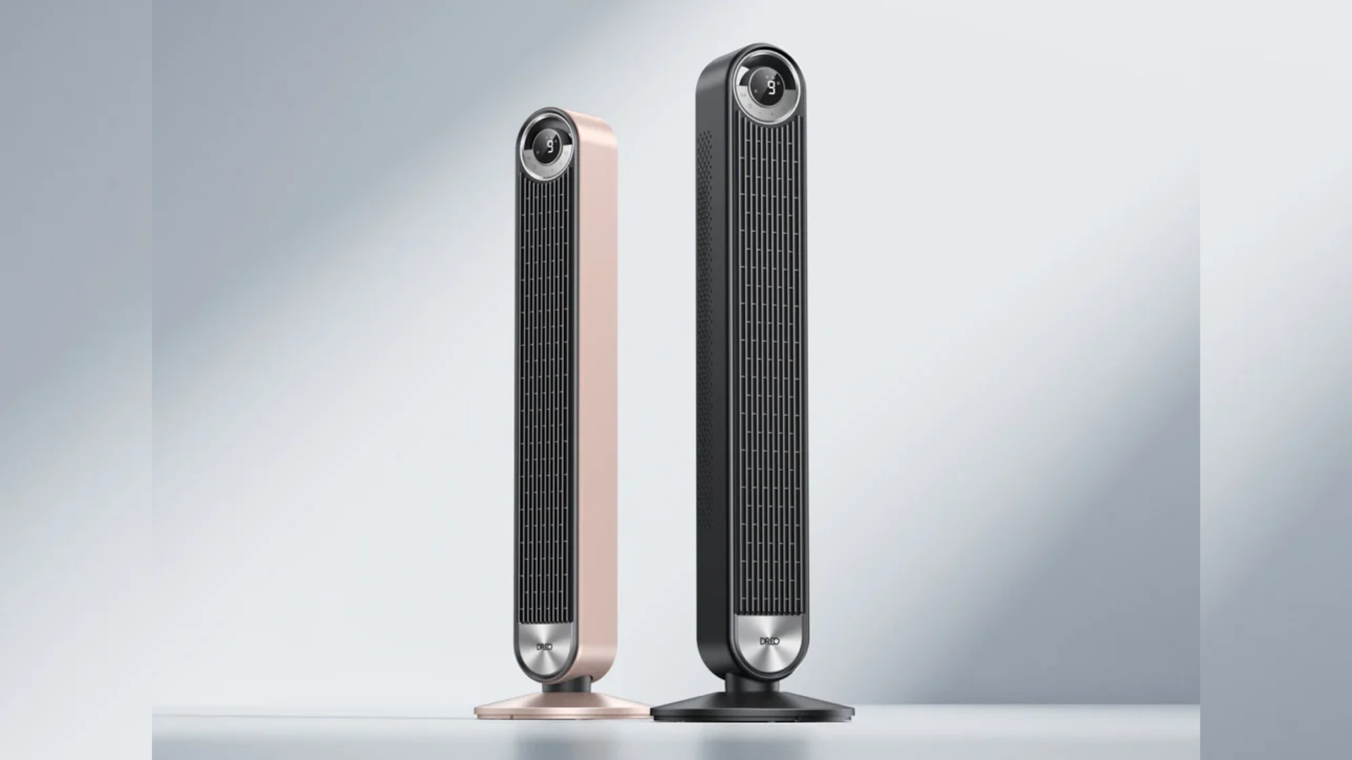 Two tall tower fans one rose gold and one black with circular control dials at the top standing on a light surface against a pale gradient background