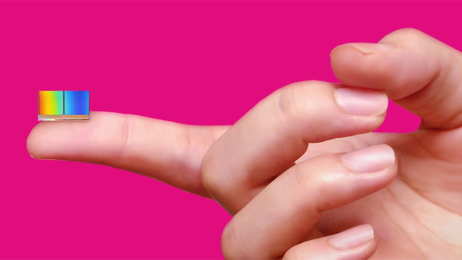 Close up of a small rainbow color swatch resting on a fingertip against a bright pink background conveying color testing