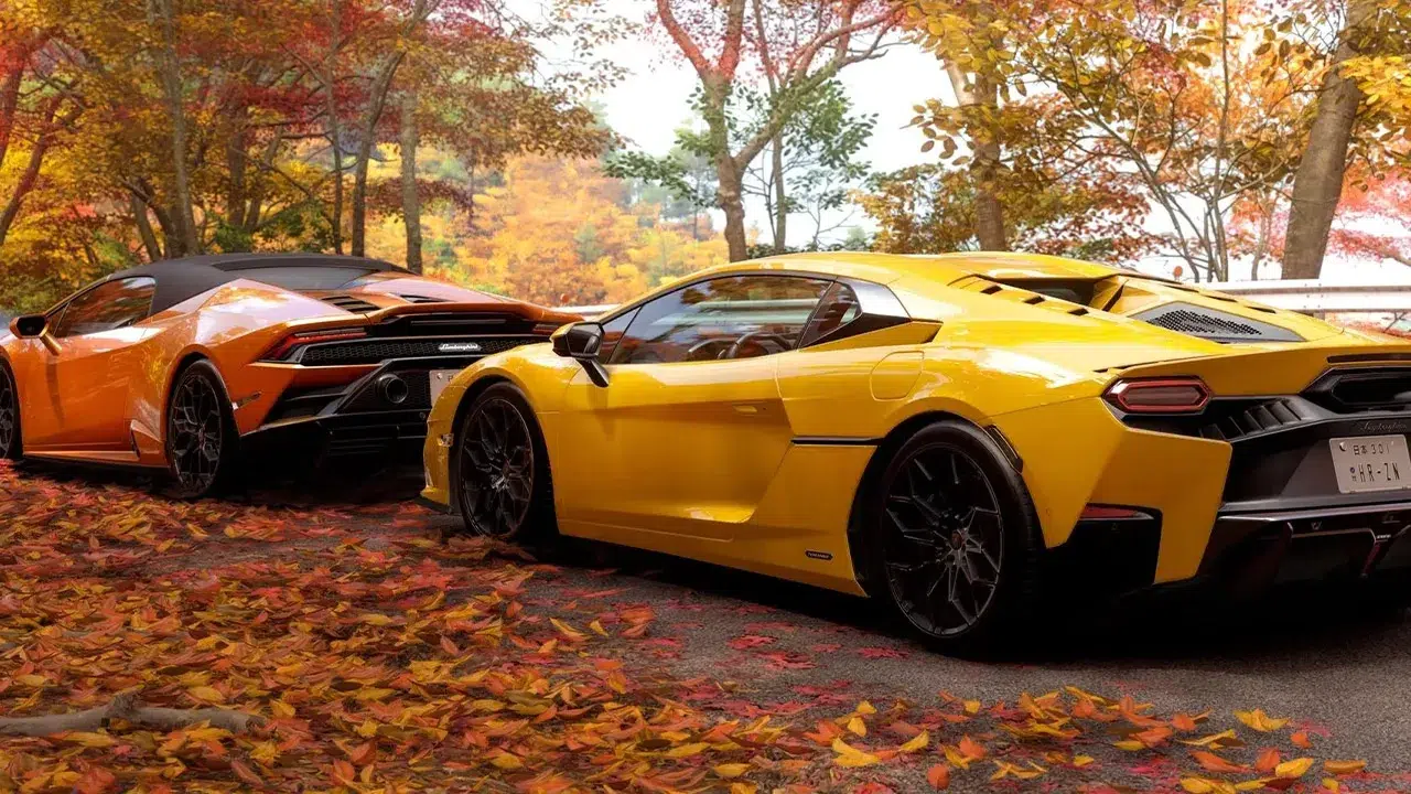 Two Lamborghini sports cars yellow and orange parked on a leaf covered road with autumn trees in the background