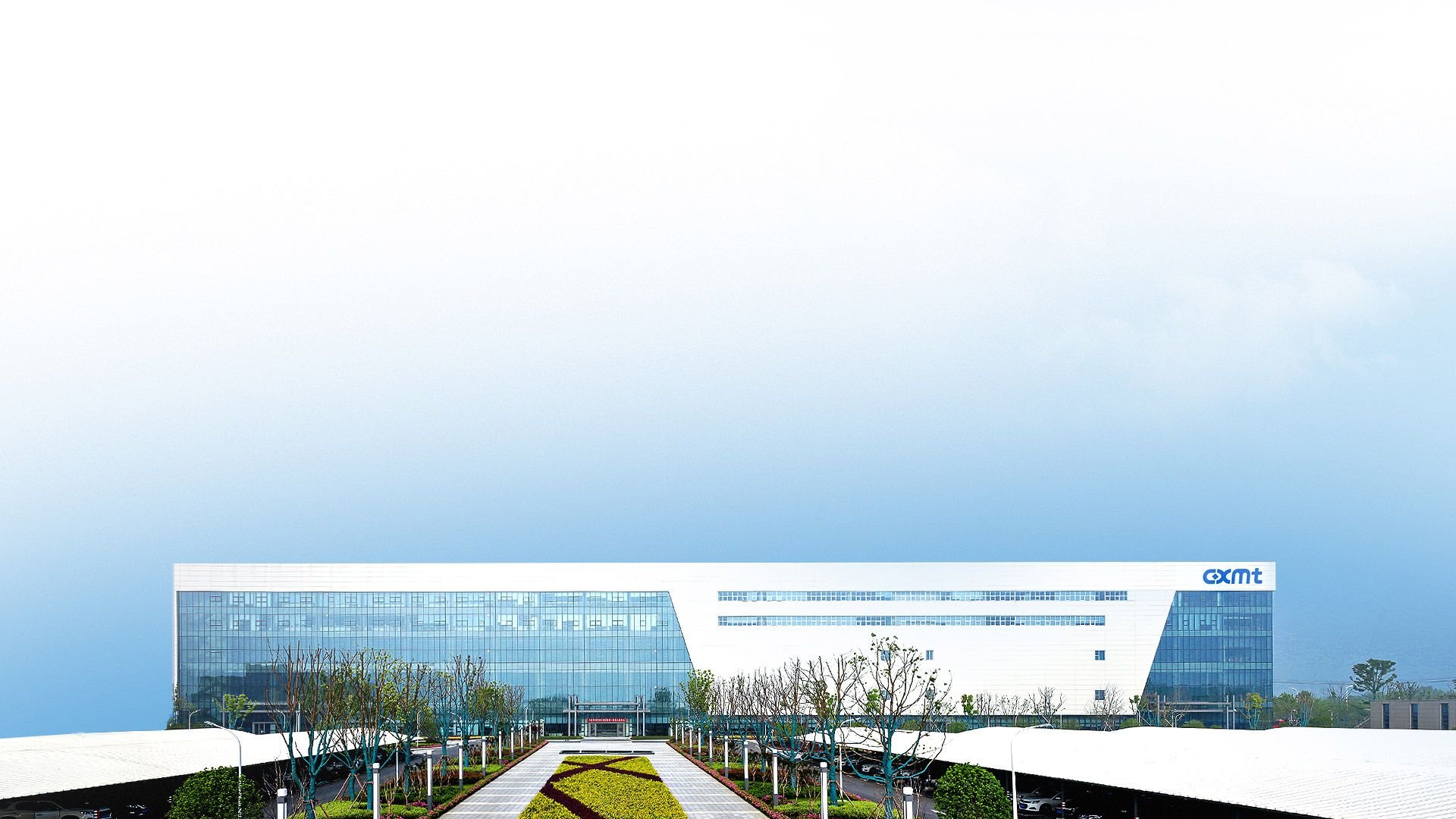 White and blue glass corporate building with a central landscaped walkway leading to the entrance set against a pale blue sky