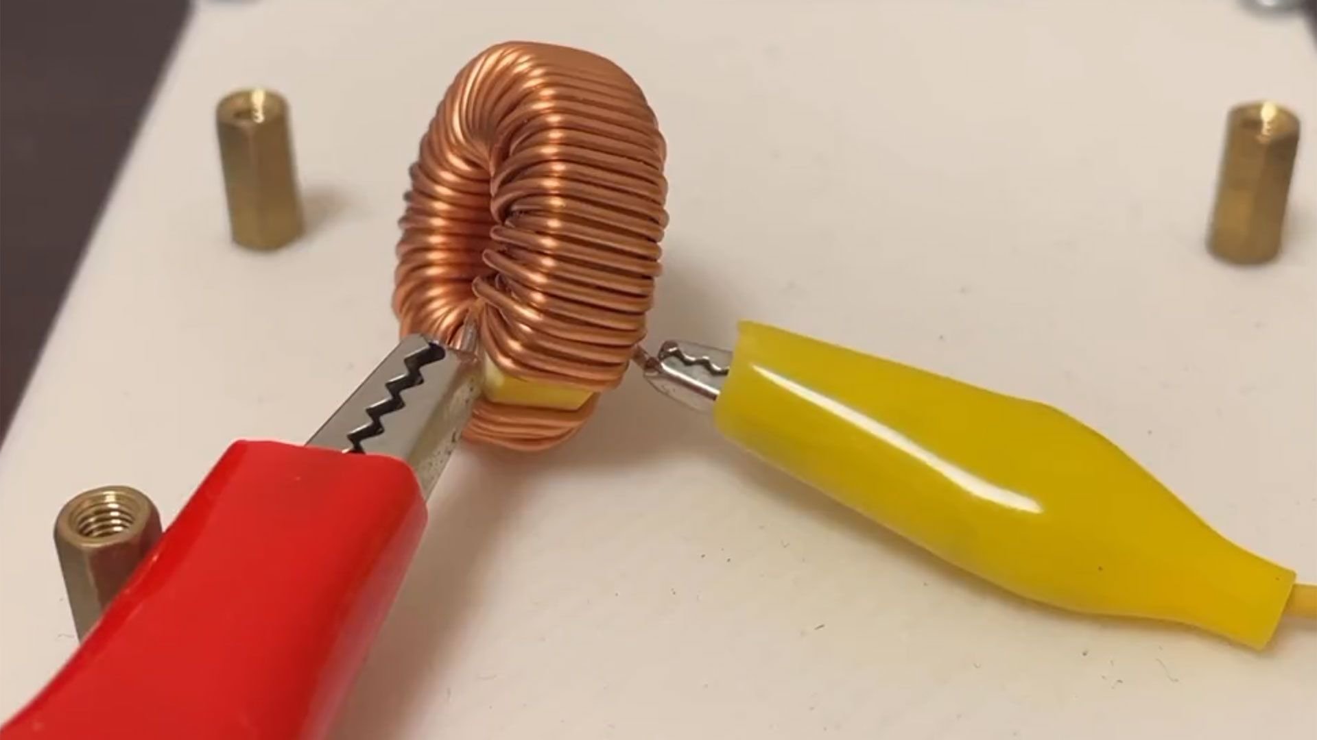 Copper wire coil solenoid clamped by alligator clips for an electrical test setup on a white surface