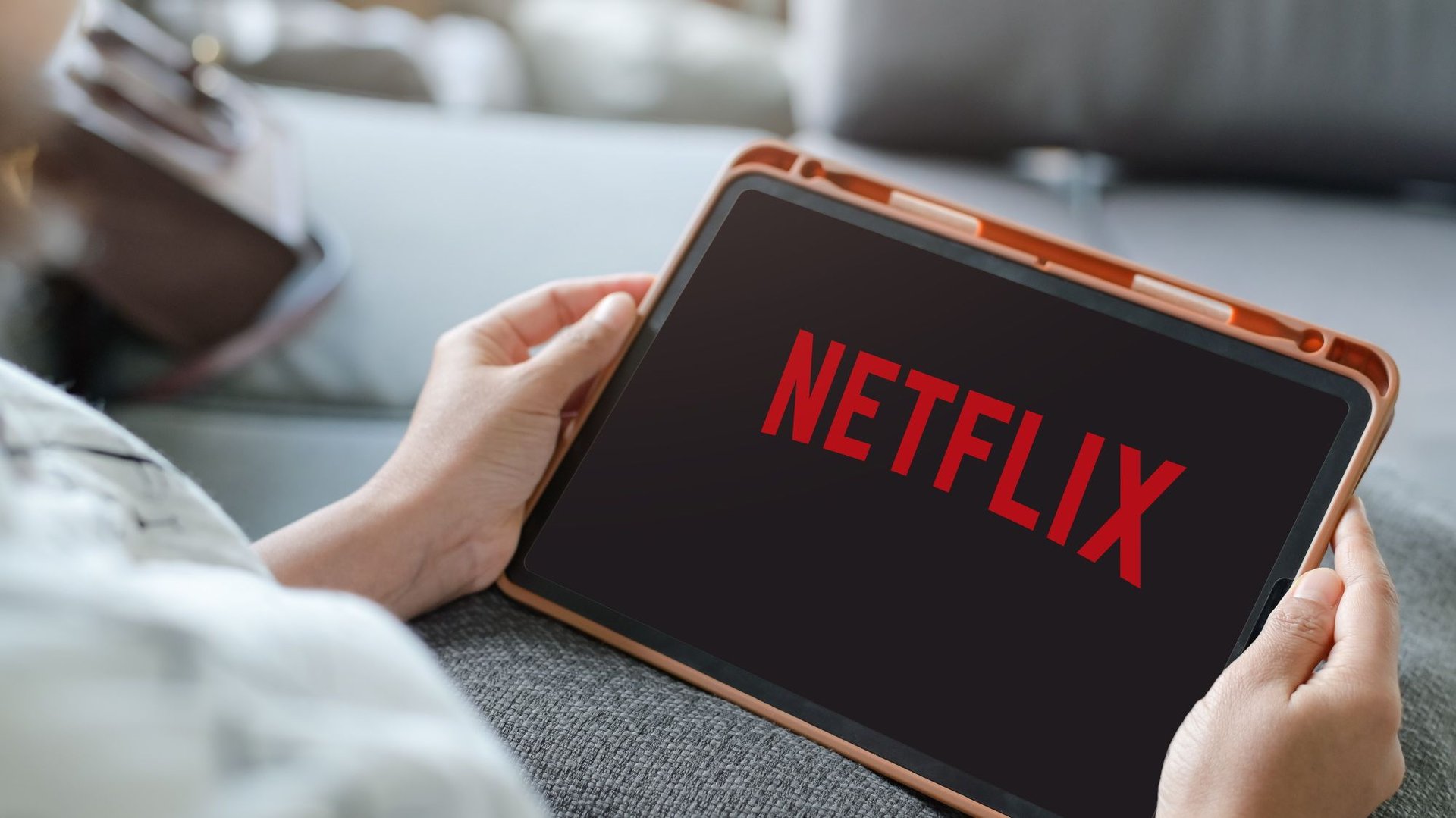 Tablet held in hands displaying the Netflix logo on screen