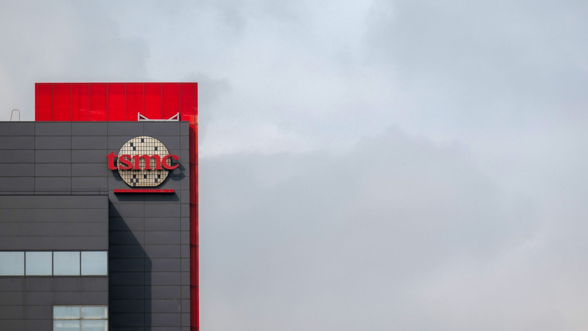 Building corner with dark gray cladding a red vertical accent and a circular tiled tsmc logo on the facade