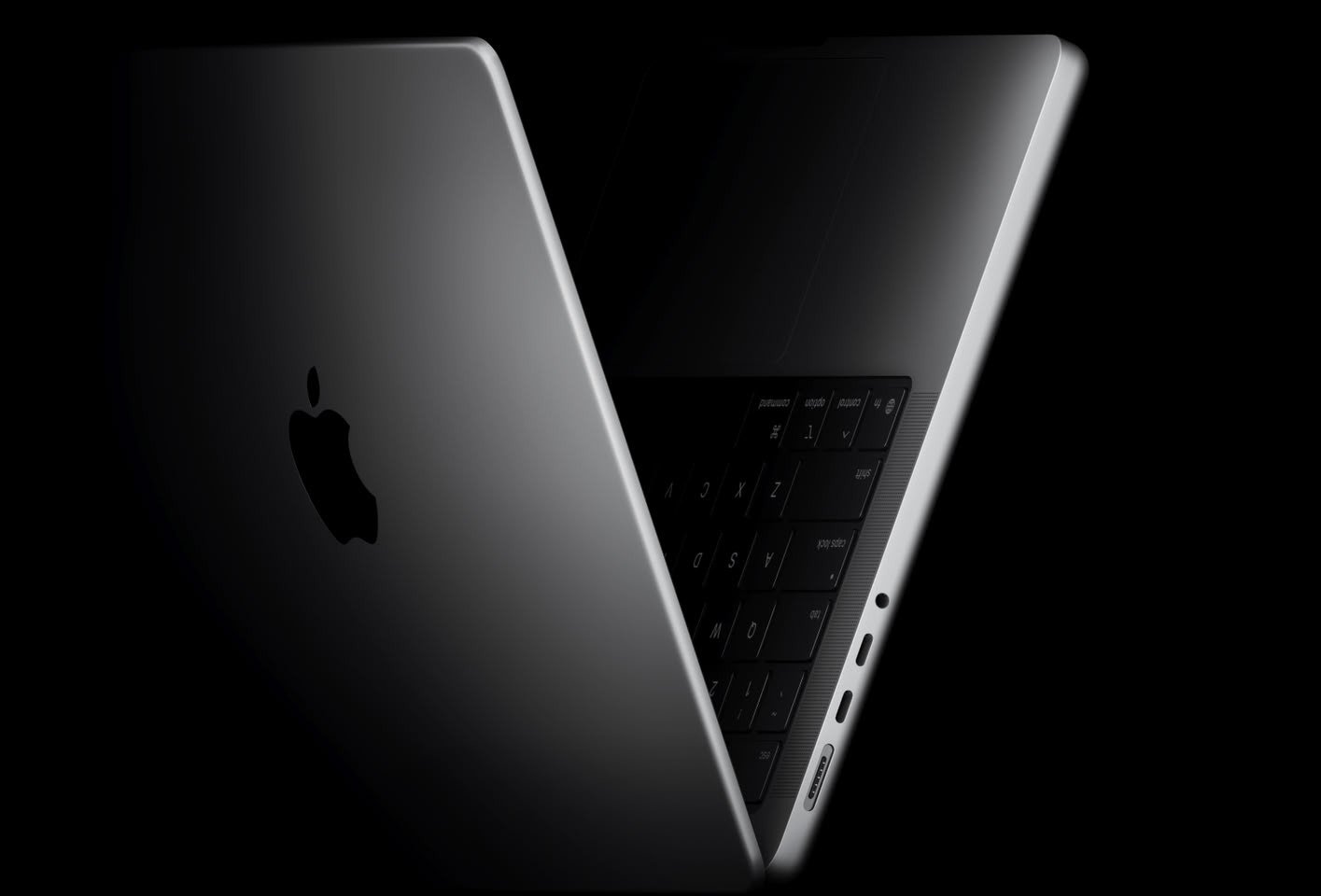Close up side view of a silver Apple MacBook Pro opened at a slight angle against a black background