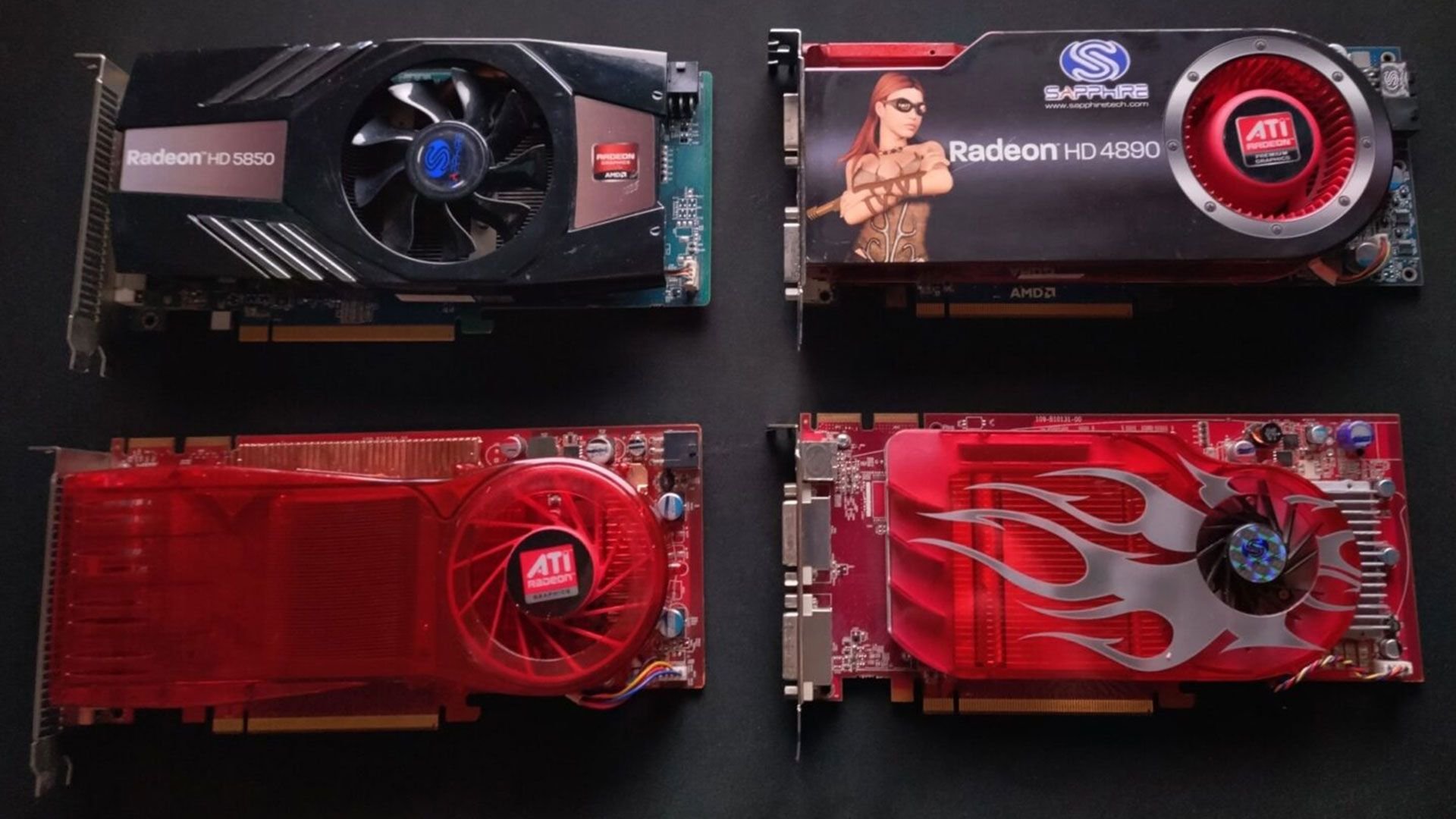 Four graphics cards laid on a dark surface showing two blackgrey GPUs at the top and two red GPUs at the bottom with labels like Radeon HD 5850 and Radeon HD 4890 visible