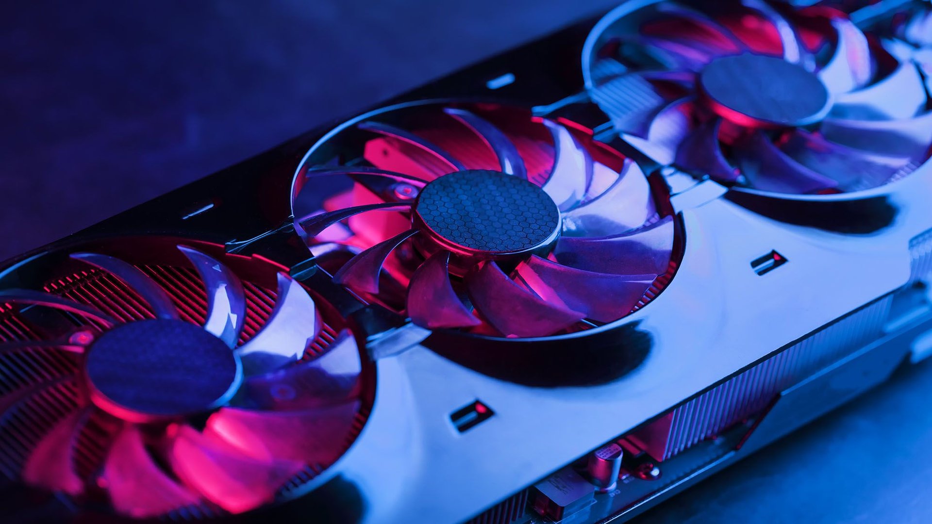 Close up of a computer graphics card with multiple illuminated cooling fans under blue and purple lighting