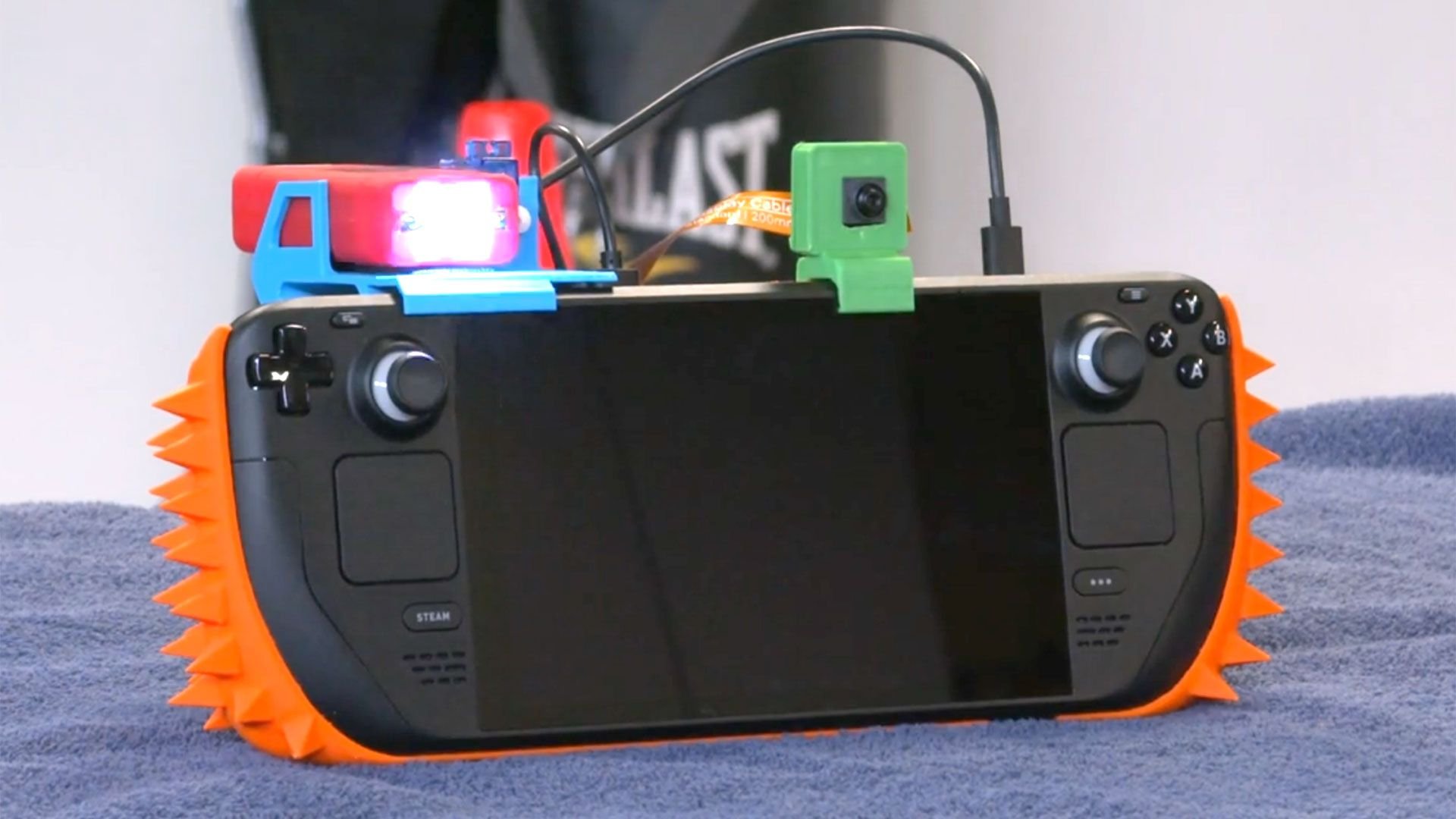Handheld gaming console with bright orange spiked side bumper and small top mounted toy accessories