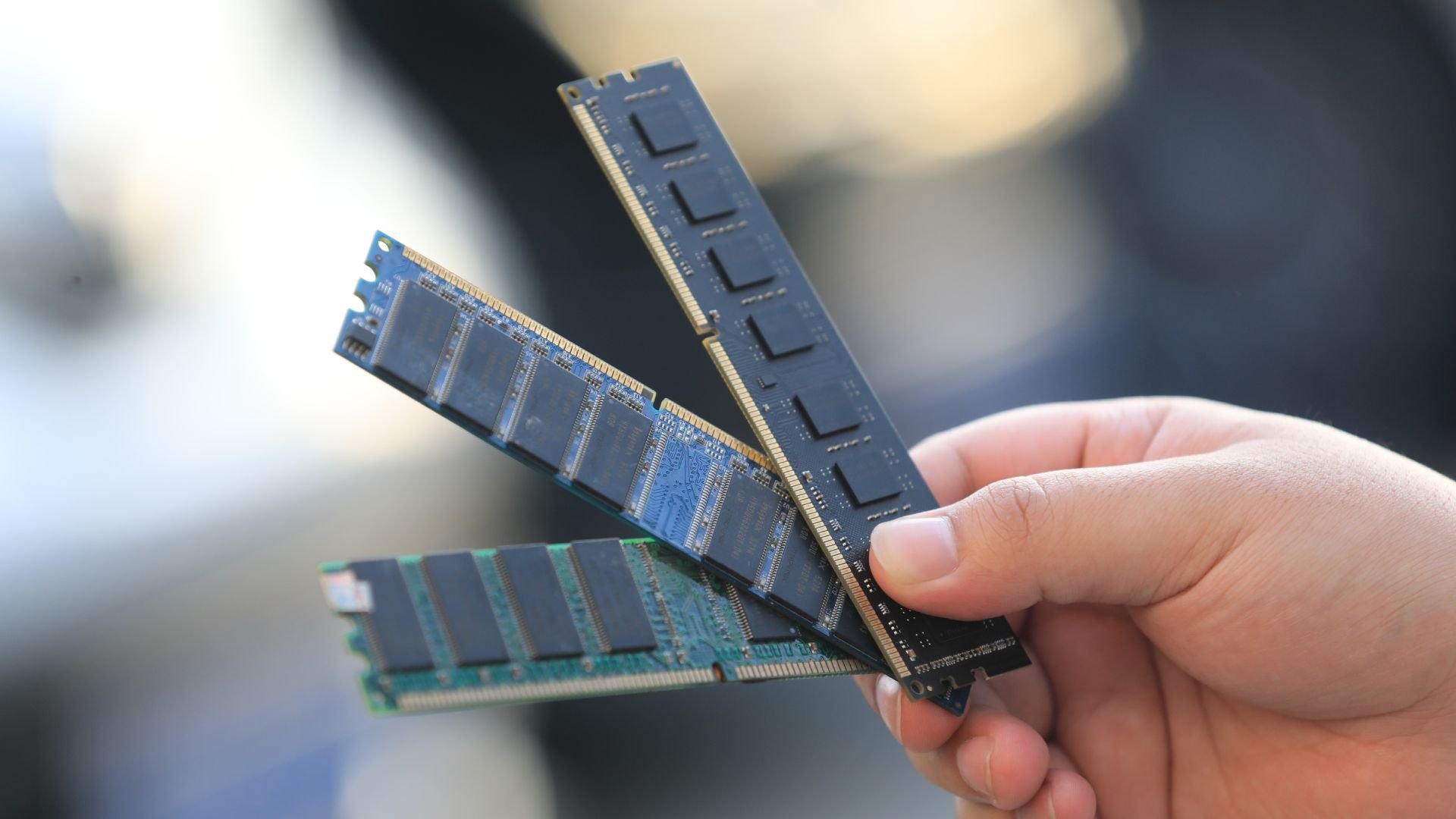 Two blue DDR RAM memory sticks being held by a hand with a blurred background close up view